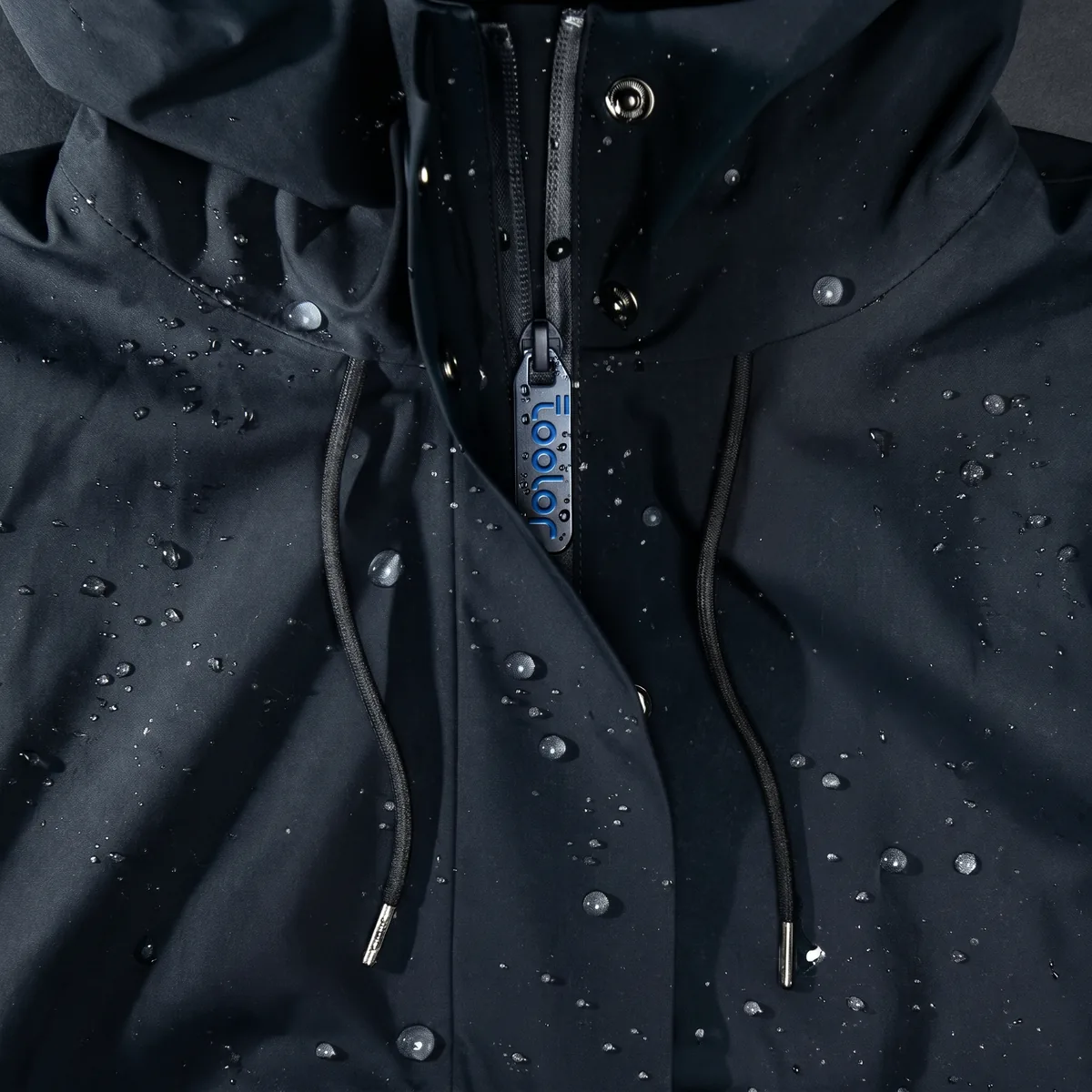Water beading and rolling off a navy Toolor waterproof shell with a cast tamga zip pull